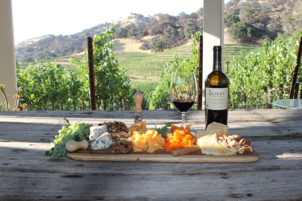 charcuterie board and bottle of Ilsley wine on a wooden table overlooking a green vineyard